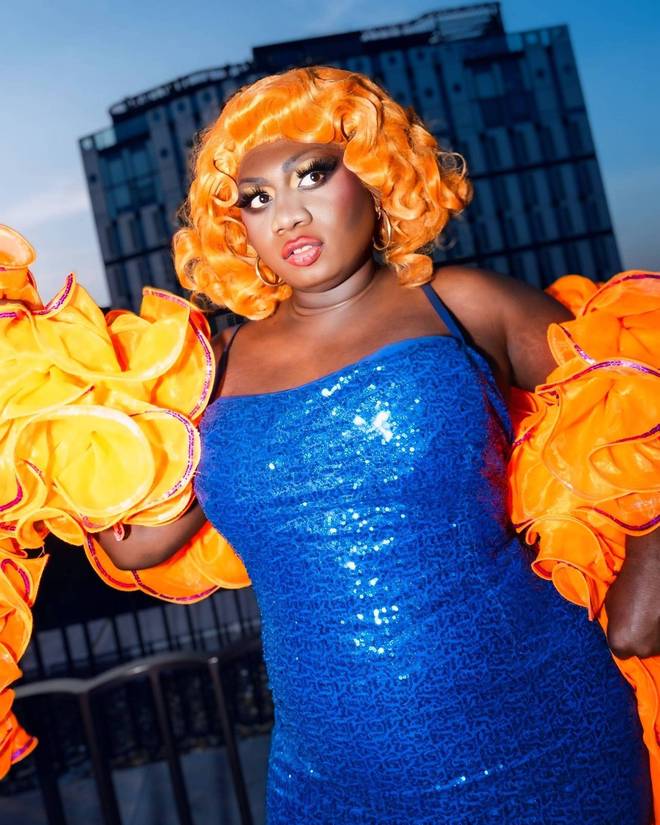 Yshee Black in a blue sequin dress, orange wig and orange ruffled boa